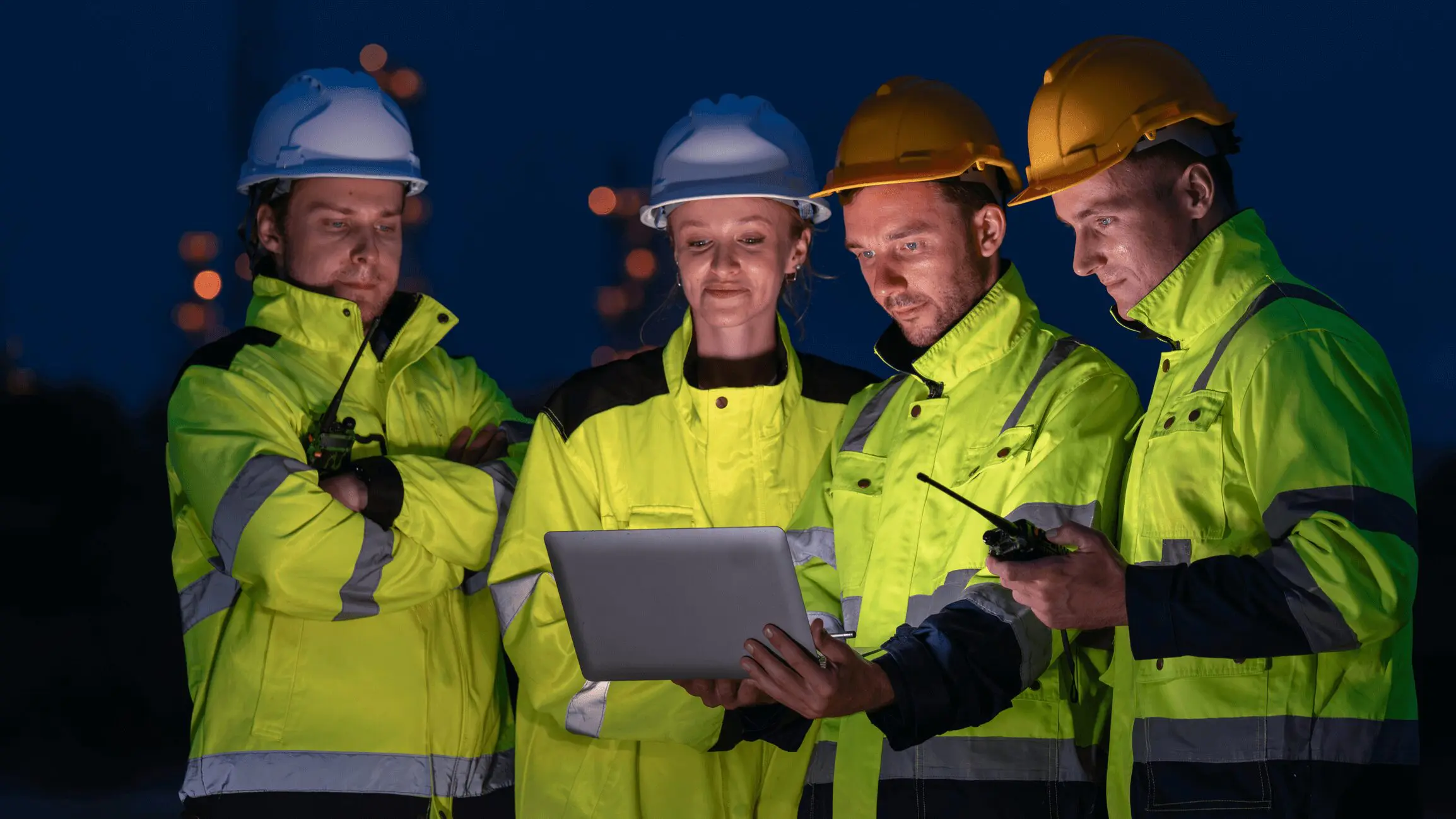 Workers in safety gear using a laptop.