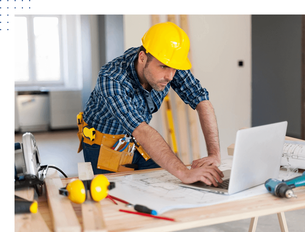 A man in yellow hard hat using laptop on table.