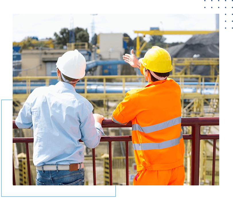 Two men in hard hats and orange jackets looking at a construction site.